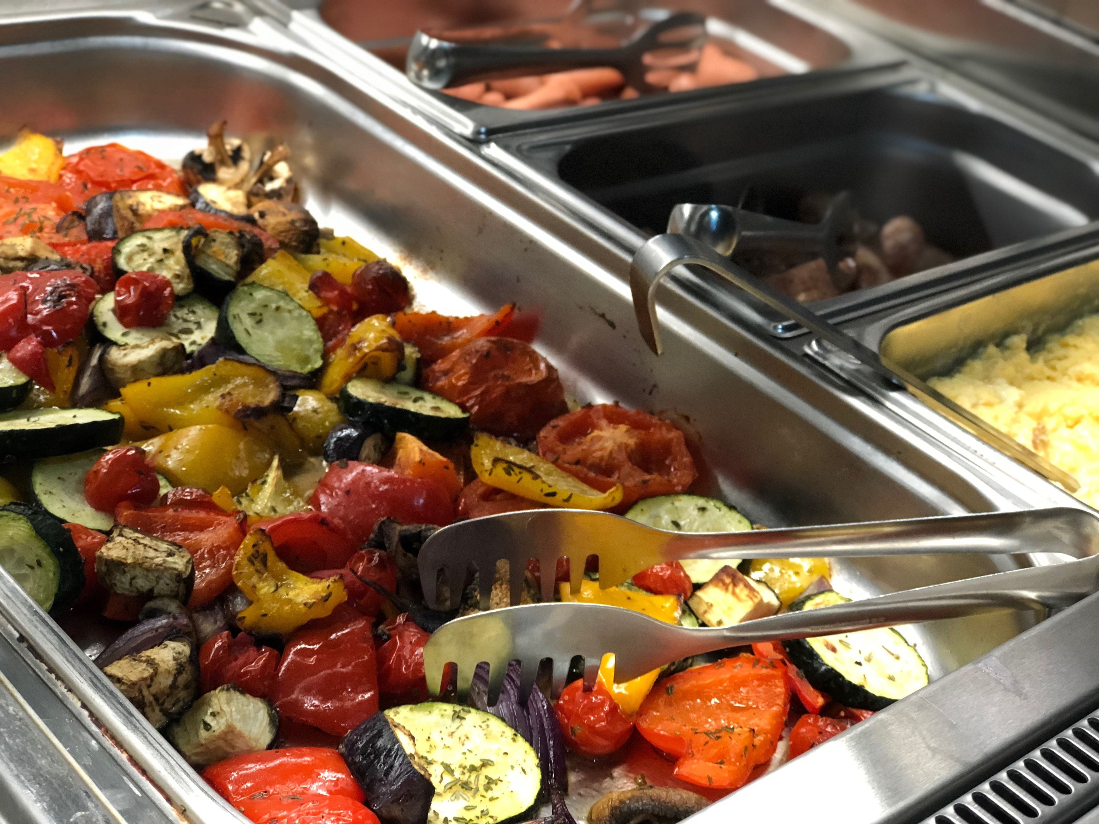 Buffet com diversos legumes cozidos e uma concha.