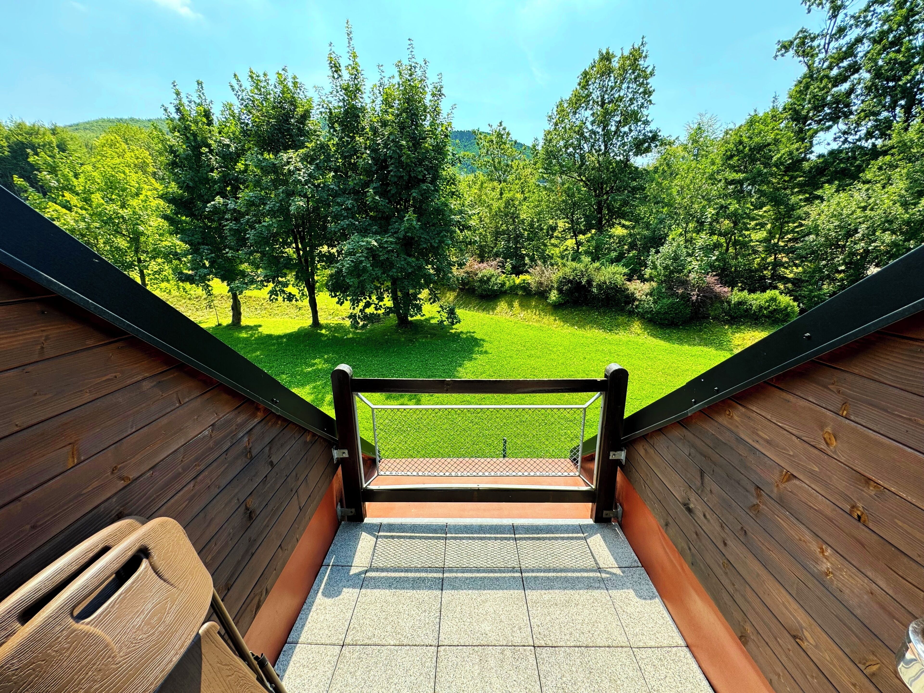 Eine Holztreppe führt zu einer grünen Fläche mit Bäumen und blauem Himmel.