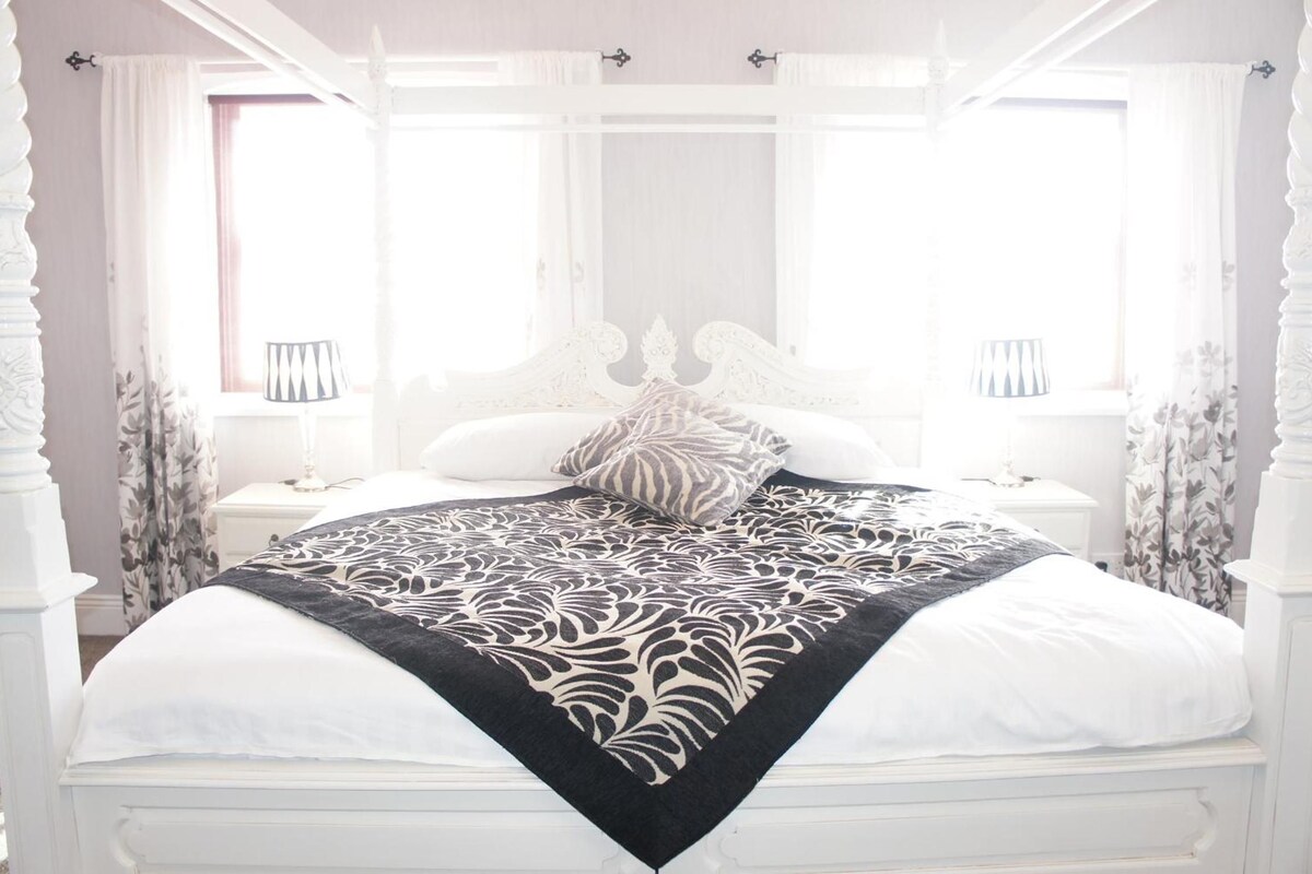 A four-poster bed with a black and white patterned bedspread, white bedding, and matching pillows.