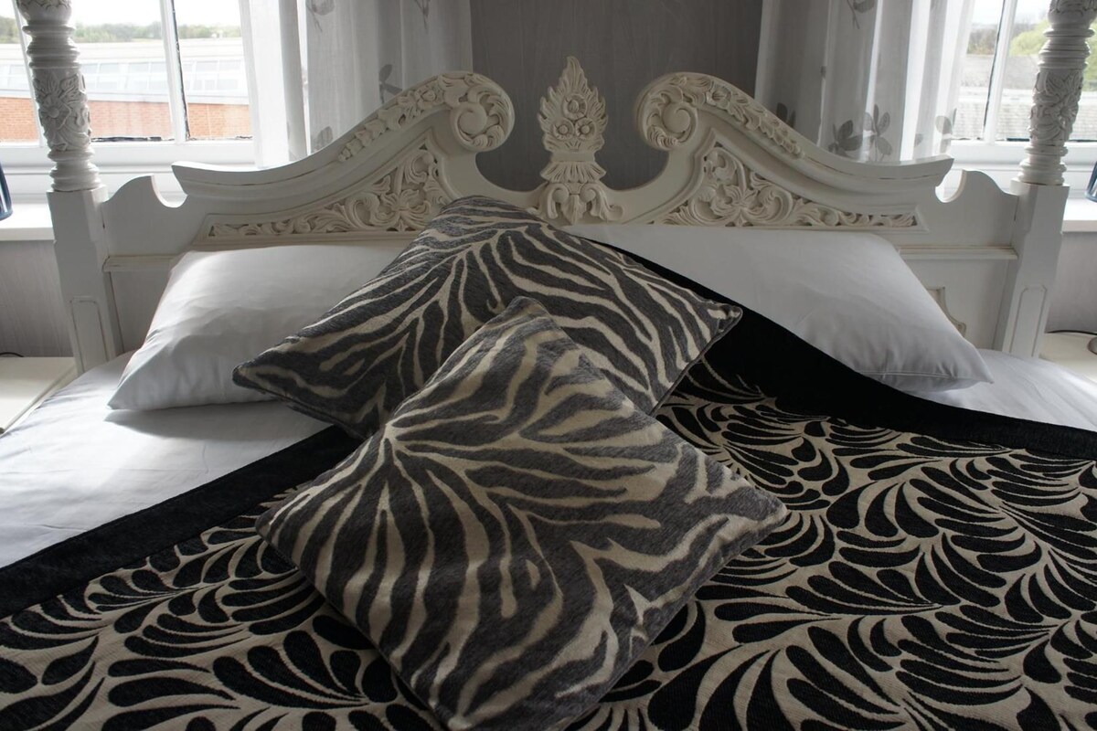 A bed with a zebra-patterned throw and pillows, a white headboard, and a window with curtains.