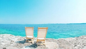 Two wooden lounge chairs facing a rocky beach with clear turquoise water. - Corfu Luxury Villas (Corfu)