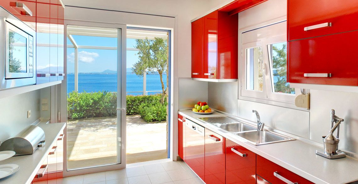 Una cocina moderna con armarios rojos, un ventanal y vista al mar.