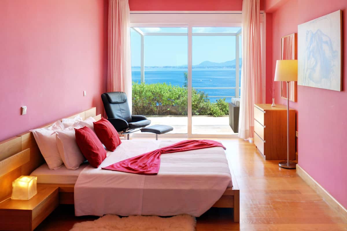 A bedroom with a bed, a chair, a bedside table, and a view of the sea.