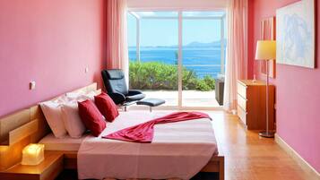 A bedroom with a bed, a chair, a bedside table, and a view of the sea.