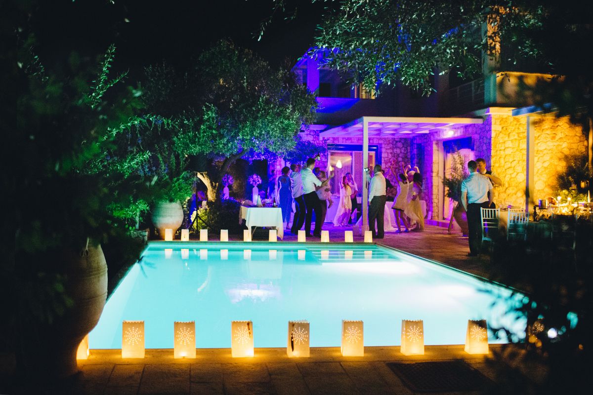 Un espace aménagé au bord de la piscine, avec un mur en pierre, un coin salon abrité et un groupe de personnes réunies autour d’une table.