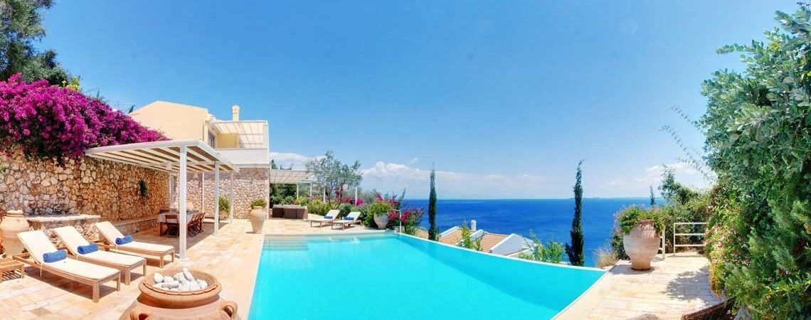 A poolside area with lounge chairs, a pergola, and a view of the sea.