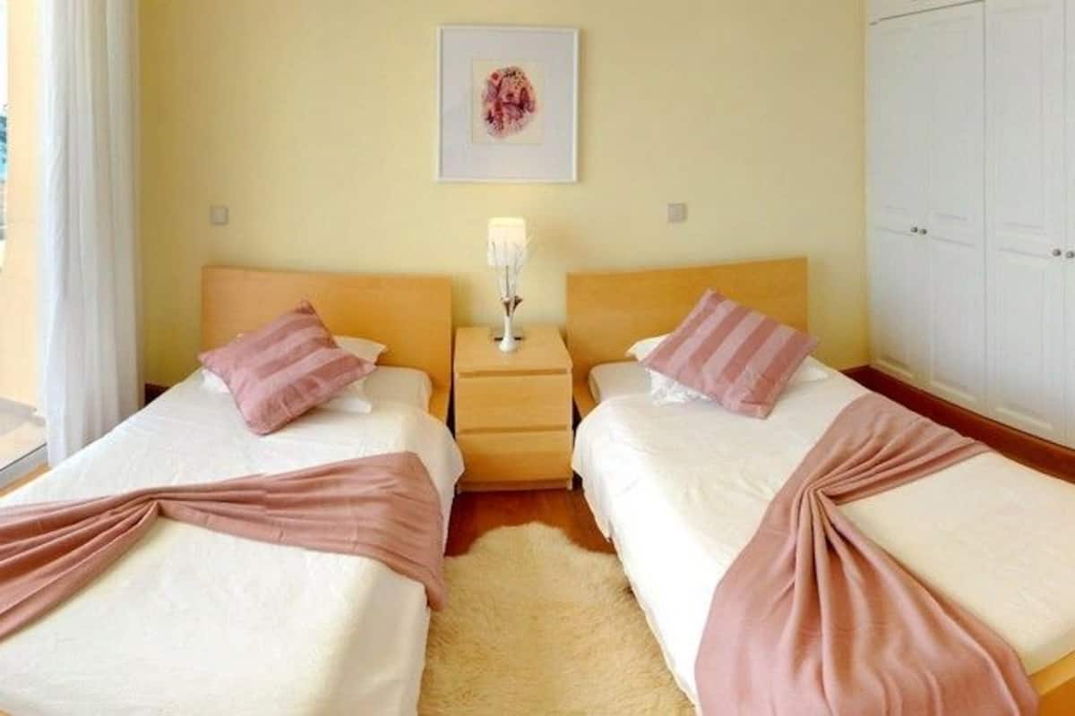 A hotel room with two beds, a balcony with a table and chairs, and a view of the sea.