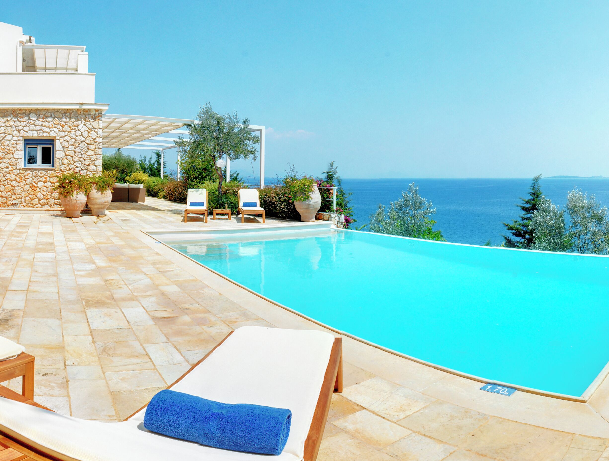 A poolside area with a clear view of the sea, stone walls, and lounge chairs.
