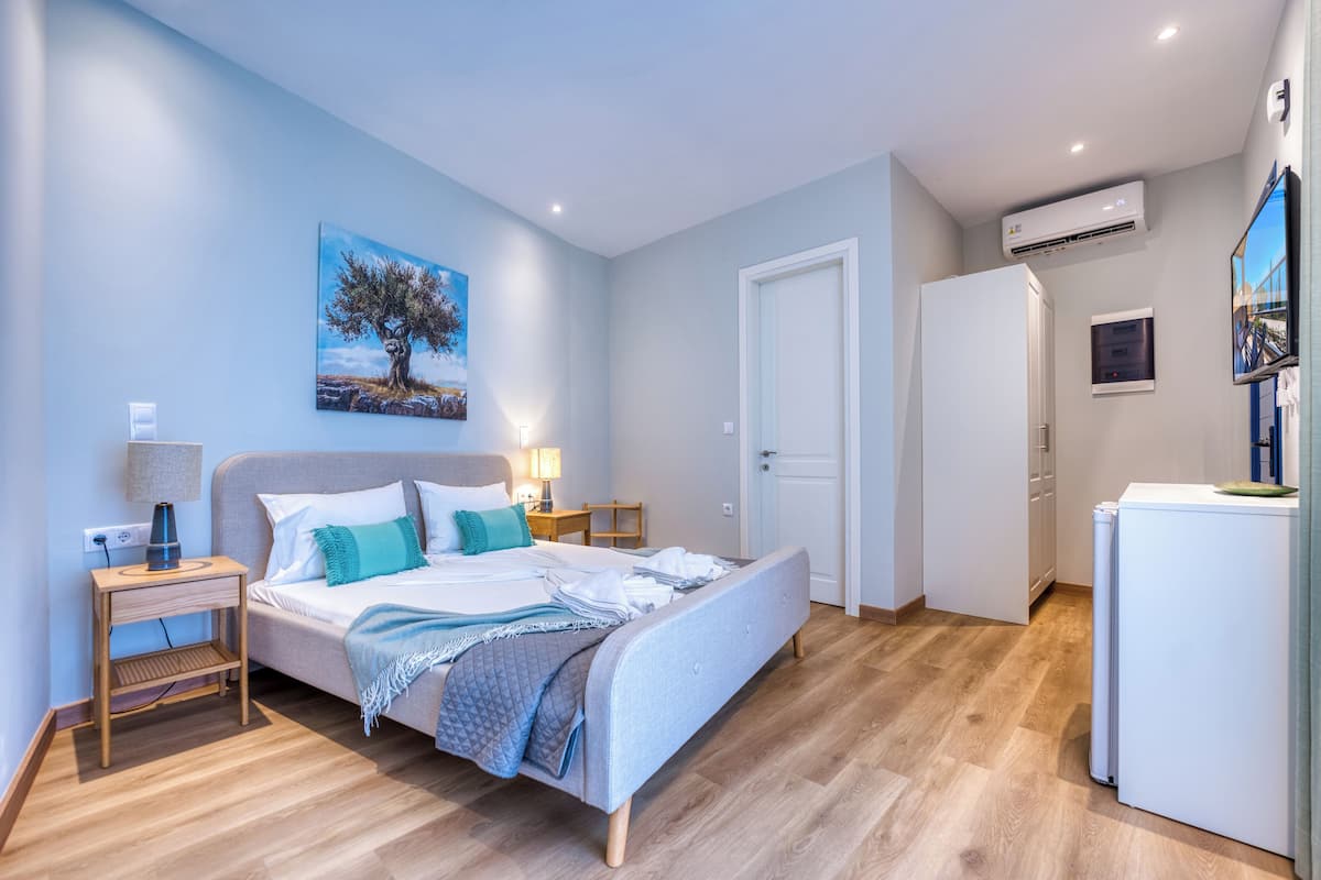 A bedroom with a bed, bedside tables, a nightstand, an air conditioning unit, a door, and a wall-mounted TV.
