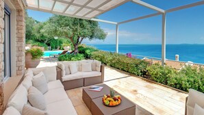 A covered outdoor seating area with a pool, a tree, and a view of the sea. - Corfu Luxury Villas (Corfu)