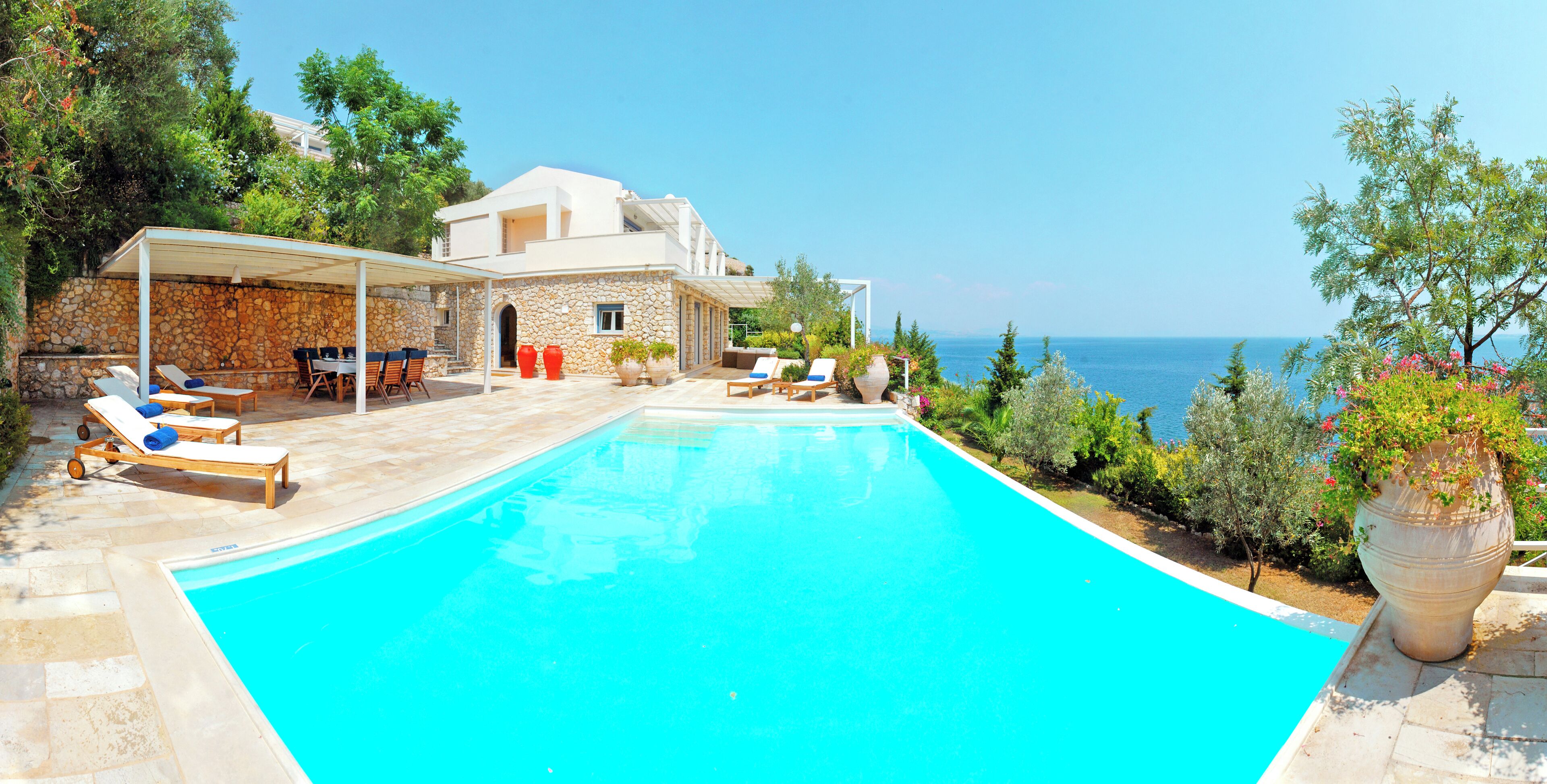 A poolside area with lounge chairs, a covered patio, and a view of the sea.