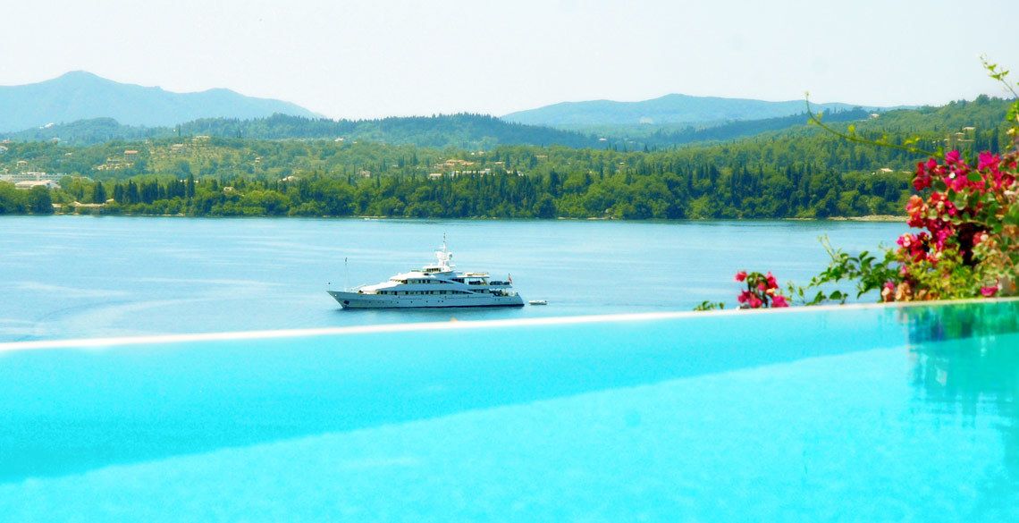 A yacht on a calm lake with a clear view of the surrounding greenery and mountains in the background.