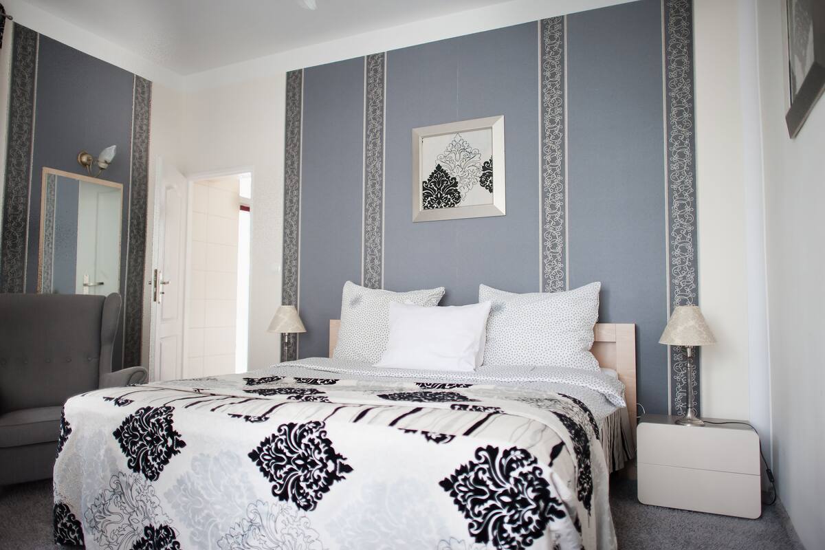 A bedroom with a bed, two bedside tables, a chair, and a mirror.