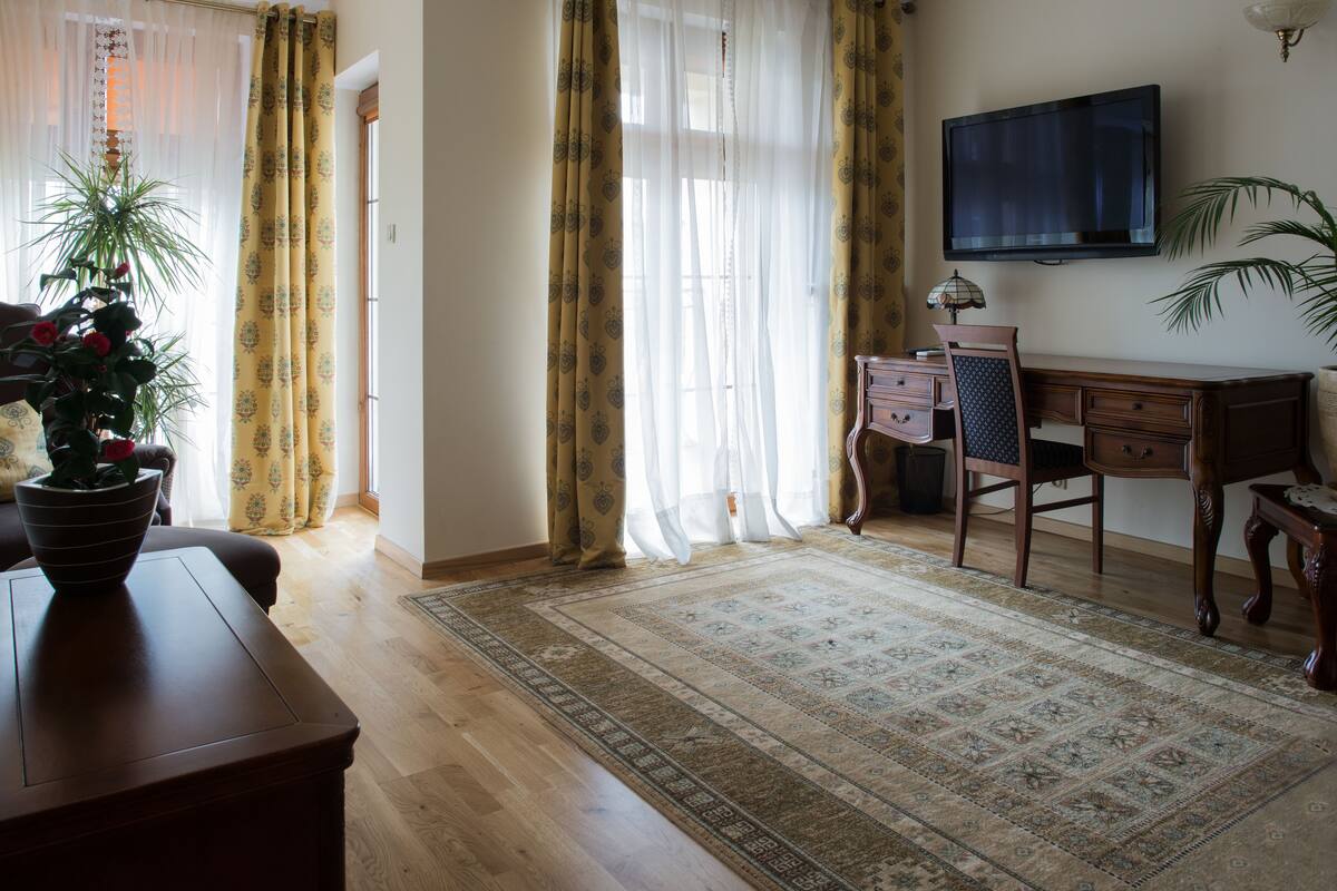 A room with a wooden desk, a television mounted on the wall, a patterned rug, and a potted plant.