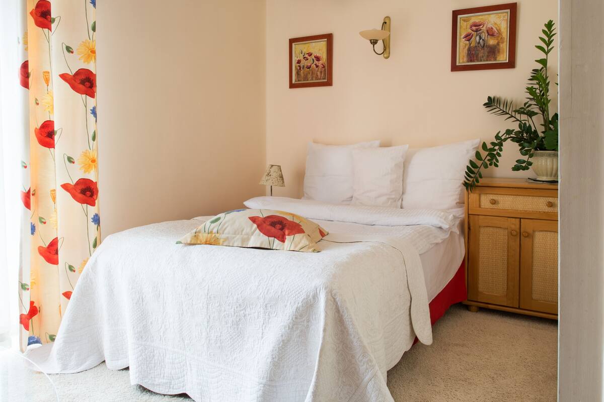 A neatly made bed with white linens, a bedside table with a lamp, and a wooden cabinet.