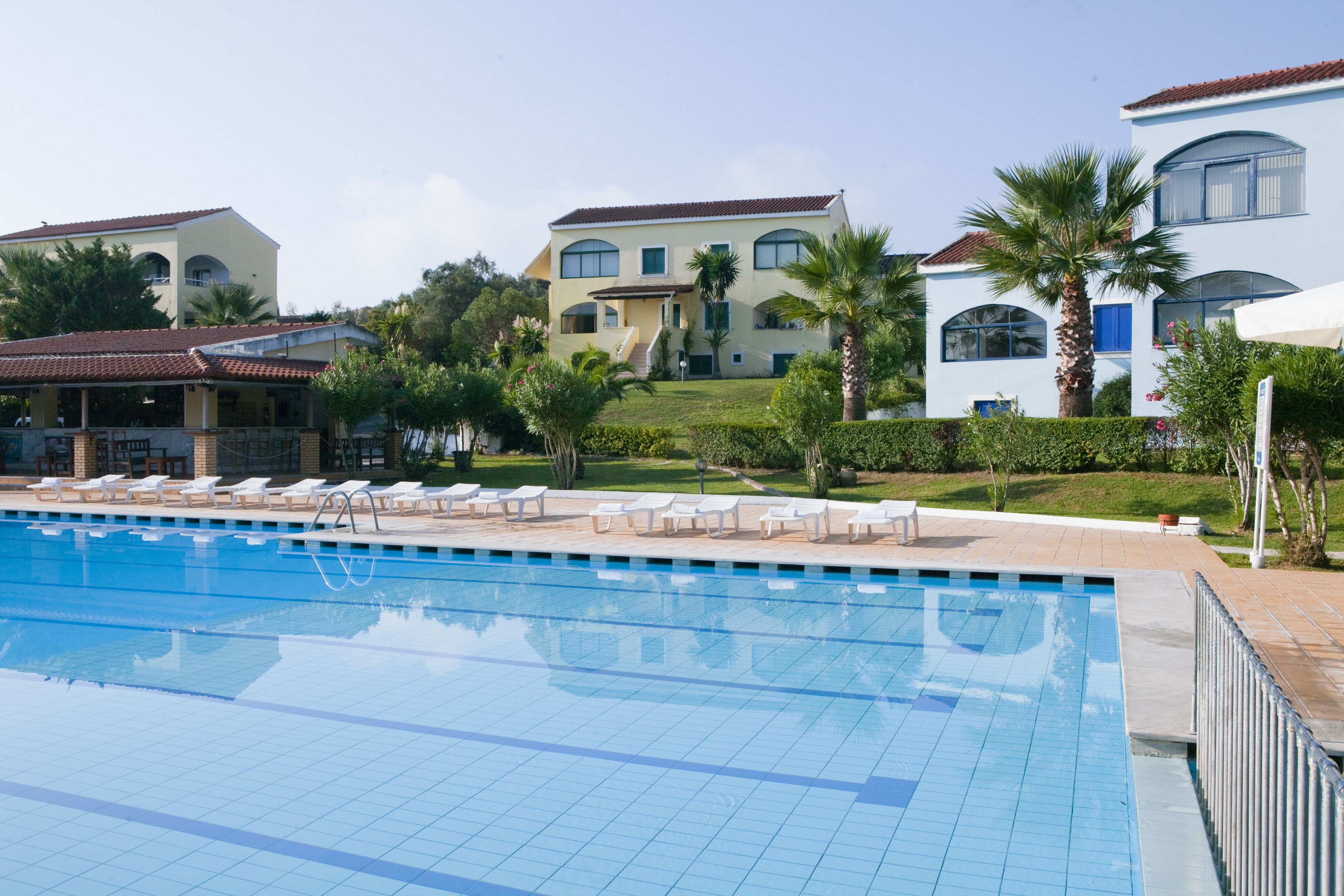 A swimming pool with lounge chairs, a building with a tiled roof, and palm trees.