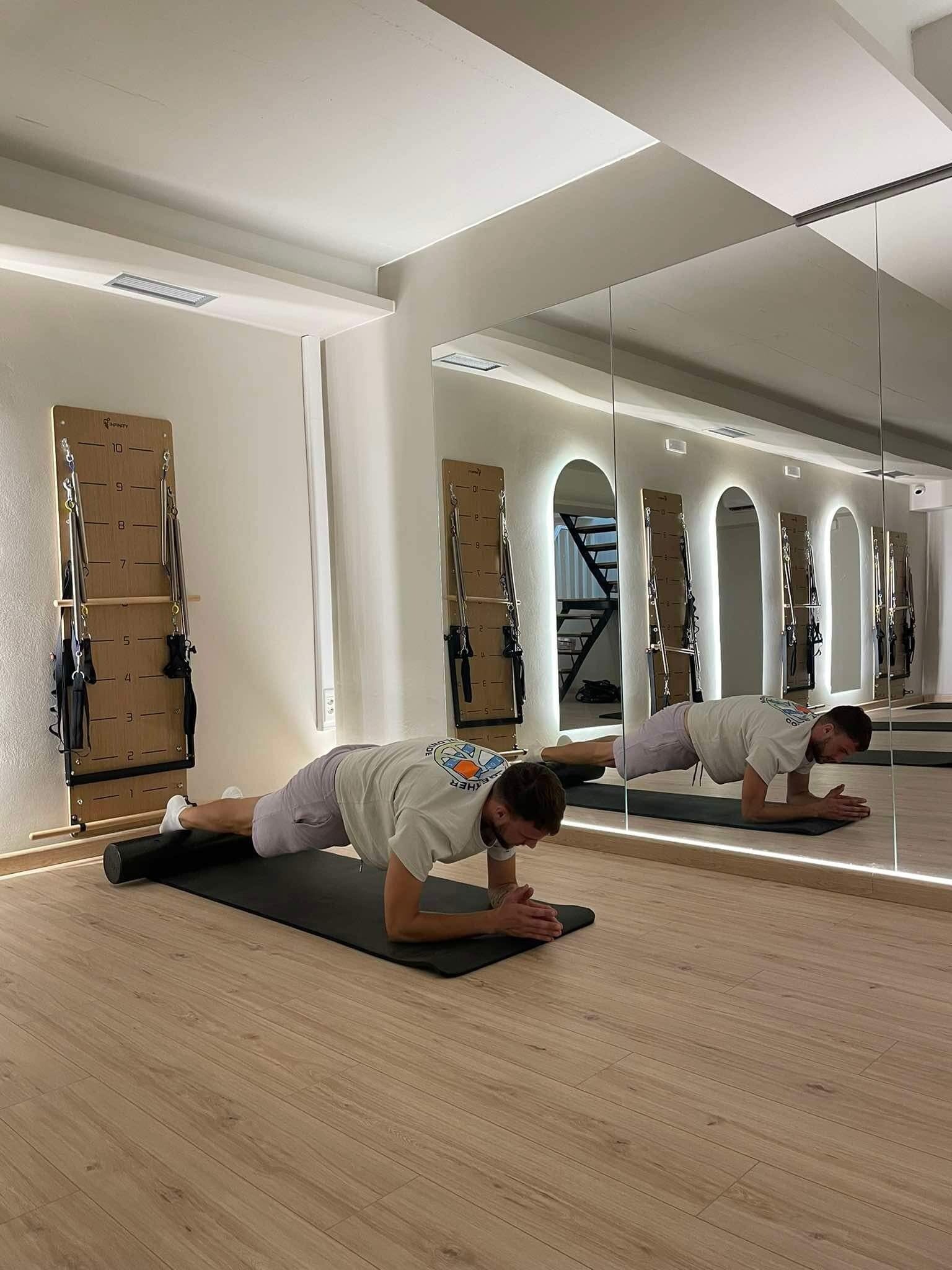 A room with a wooden floor, a black exercise mat, and a Pilates reformer machine.
