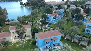 A residential area with blue and yellow houses, a central blue house with a red roof, and a lake in the background. - Govino Bay (Corfu)