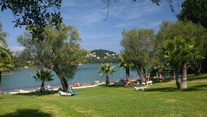A lakeside park with grassy areas, palm trees, and a view of a lake and distant buildings. - Govino Bay (Corfu)