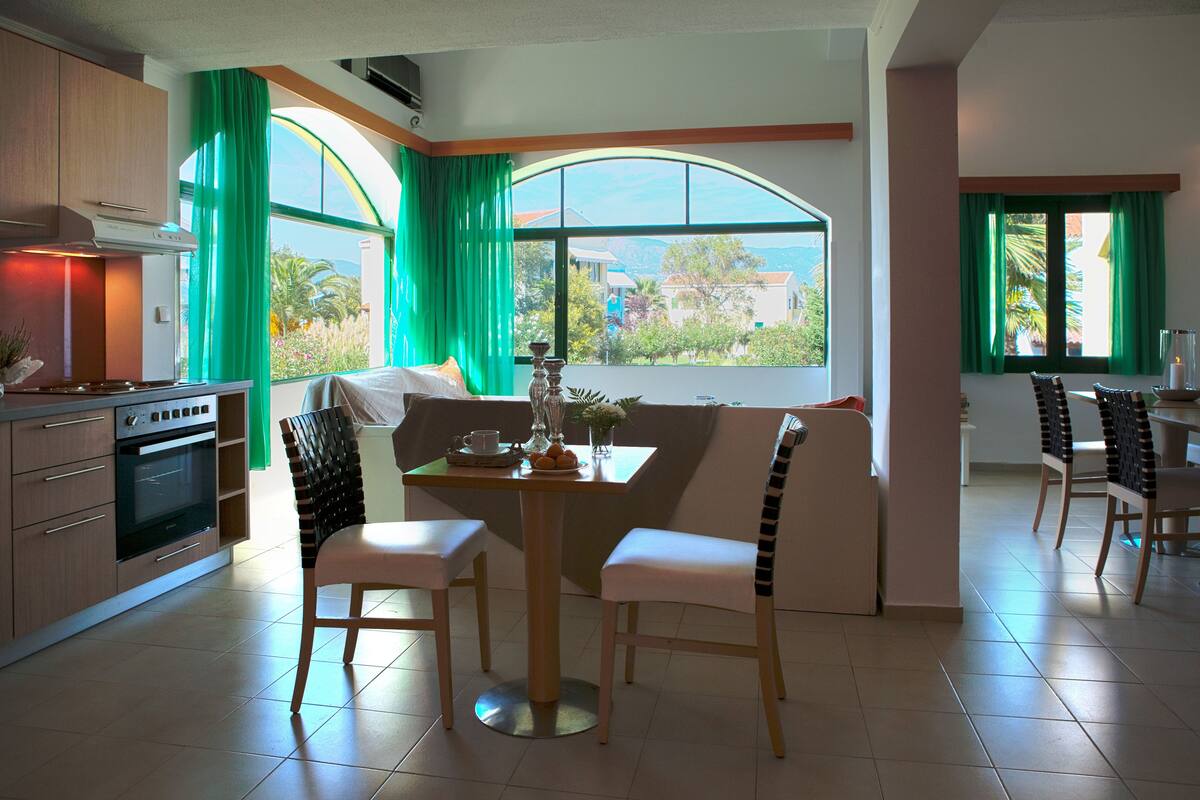 Una cocina moderna con comedor, ventanas amplias con cortinas verdes y vista del paisaje circundante.