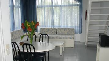 A dining area with a table, chairs, a vase with flowers, a sofa with floral upholstery, and a staircase.