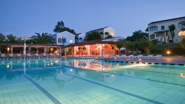 A swimming pool with lounge chairs and a building with arched windows in the background. - Govino Bay (Corfu)