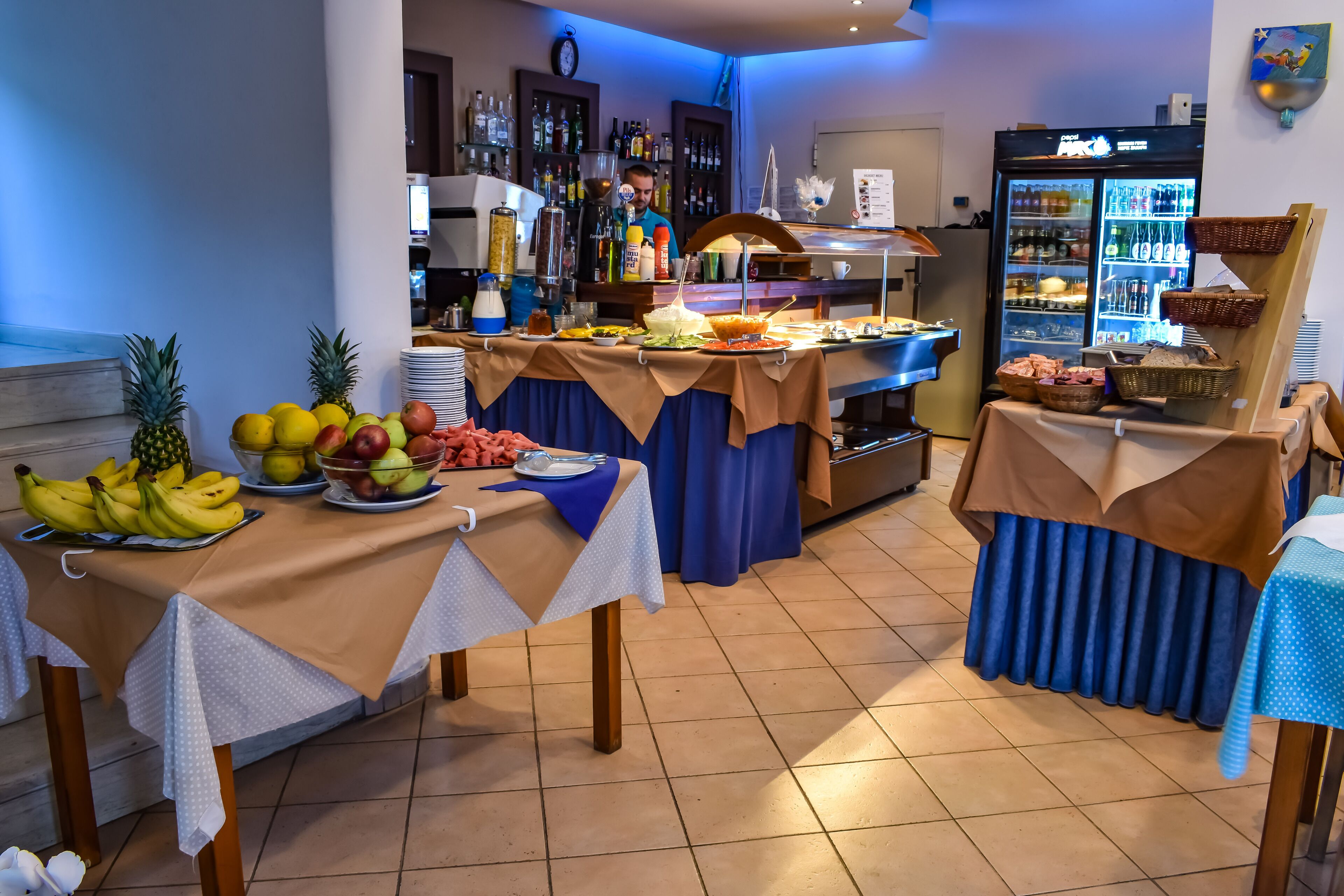 Un buffet proposant une variété de fruits et de boissons, un réfrigérateur rempli de boissons et un coin bar avec des bouteilles.