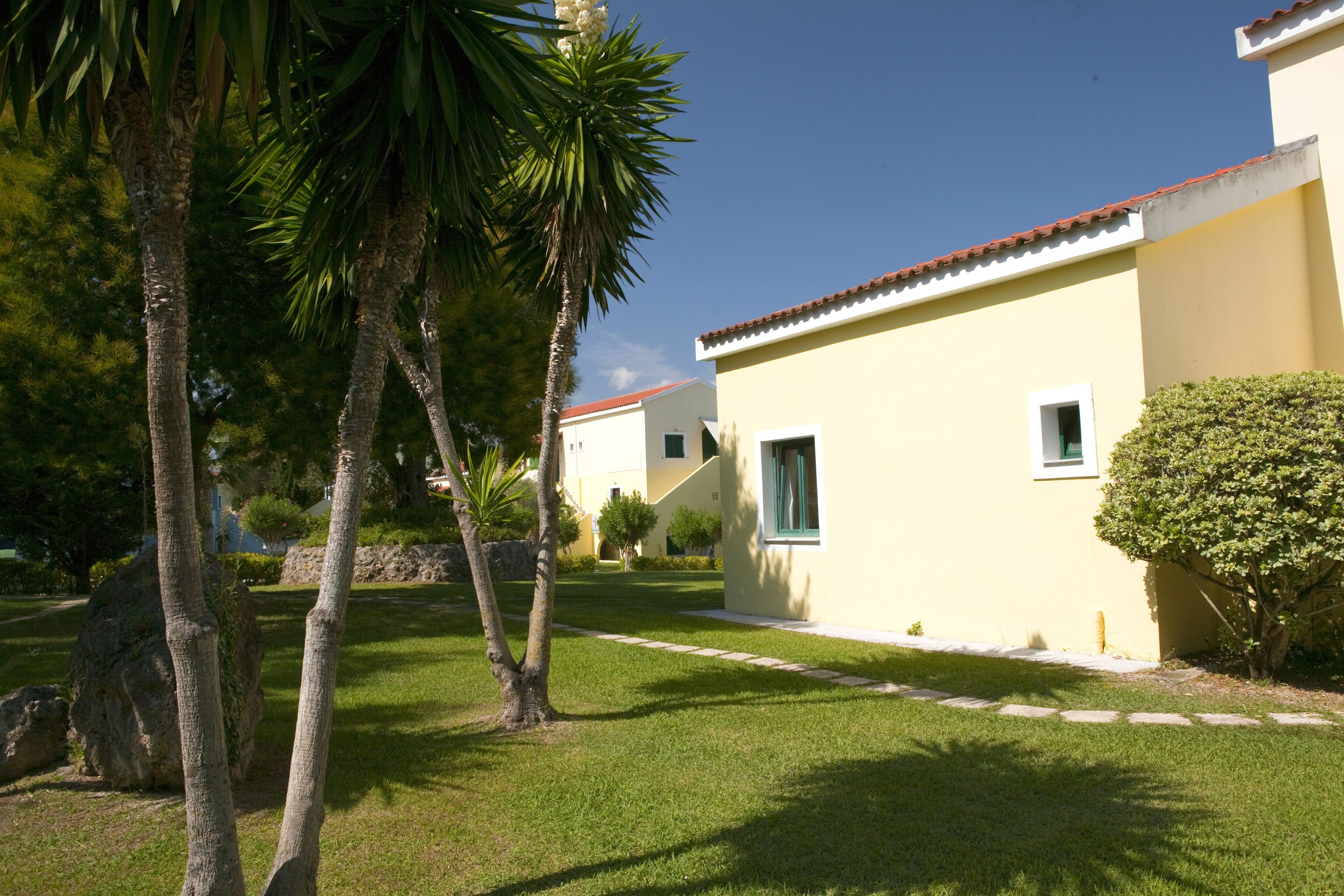 A yellow building with a red roof, surrounded by well-maintained grass and palm trees.