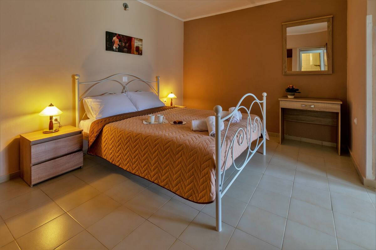 Un dormitorio ordenado con cama, mesitas de noche, cómoda y espejo.