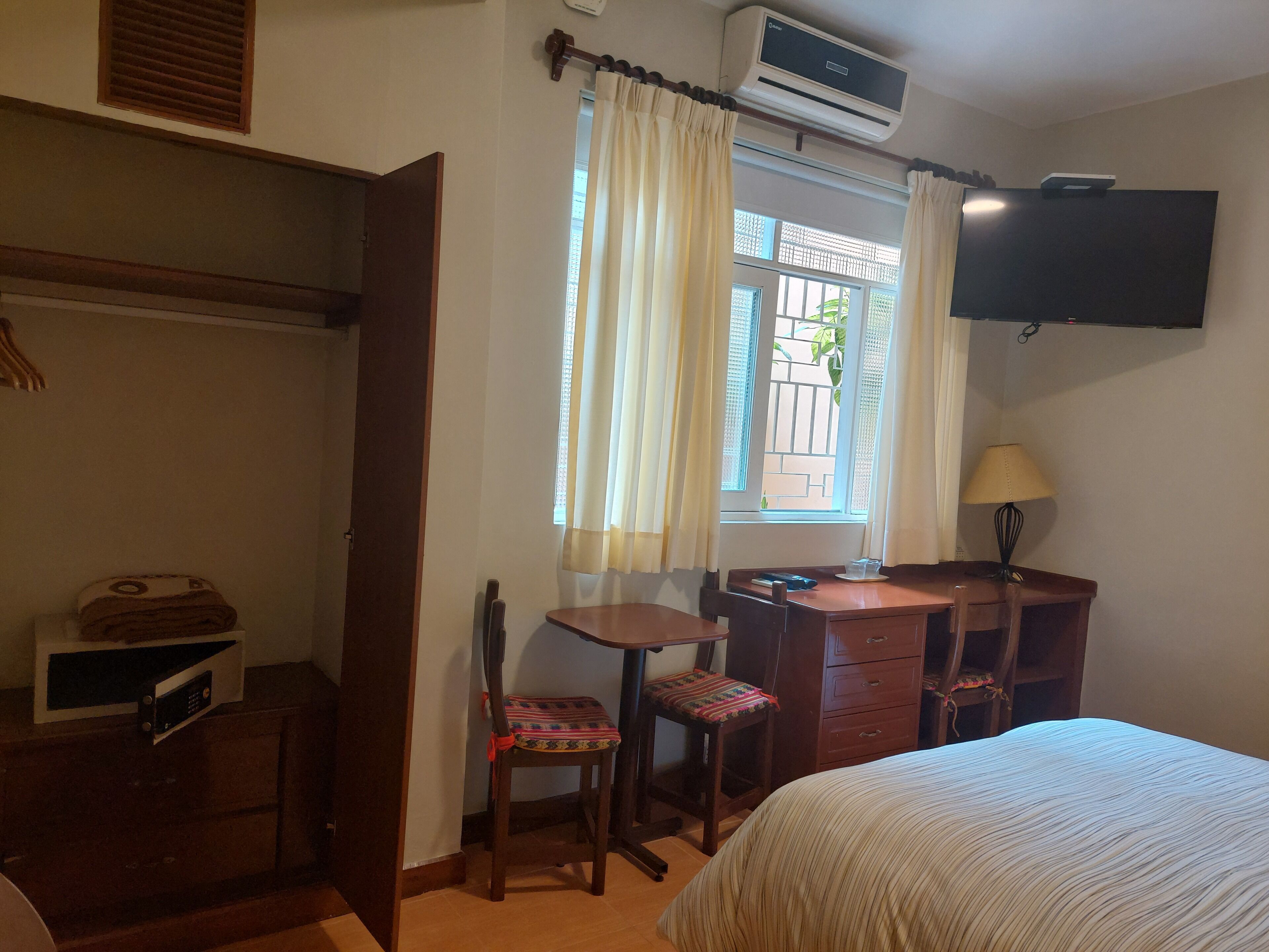 Una camera d'albergo con un letto, una scrivania con una sedia, una TV a parete e un condizionatore d'aria.