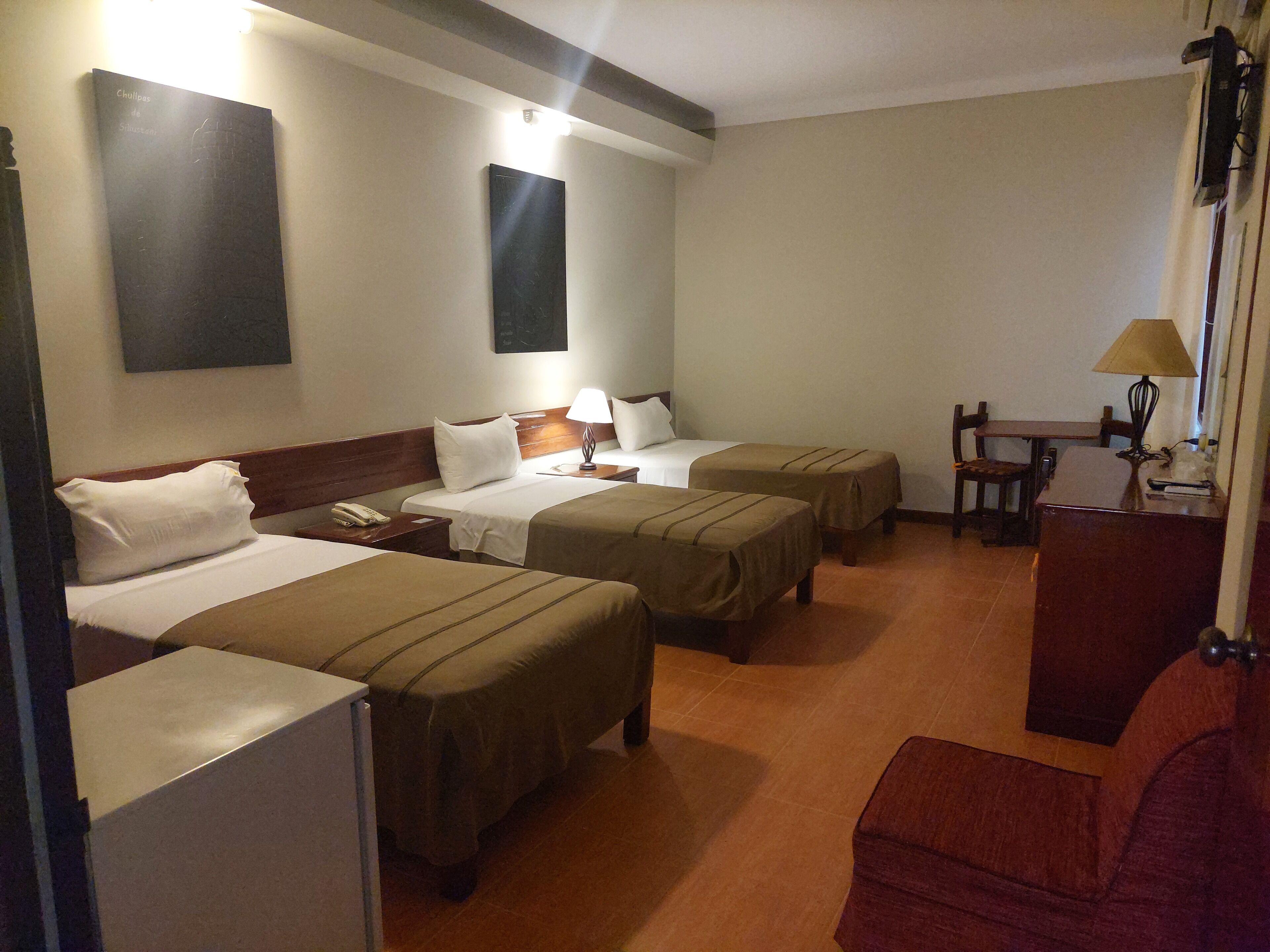 A hotel room with two single beds, a small table with a lamp, and a chair.