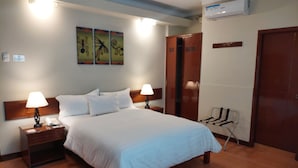 Habitación de hotel con una cama grande, dos mesitas de noche con lámparas, un armario y un aire acondicionado instalado en la pared.
