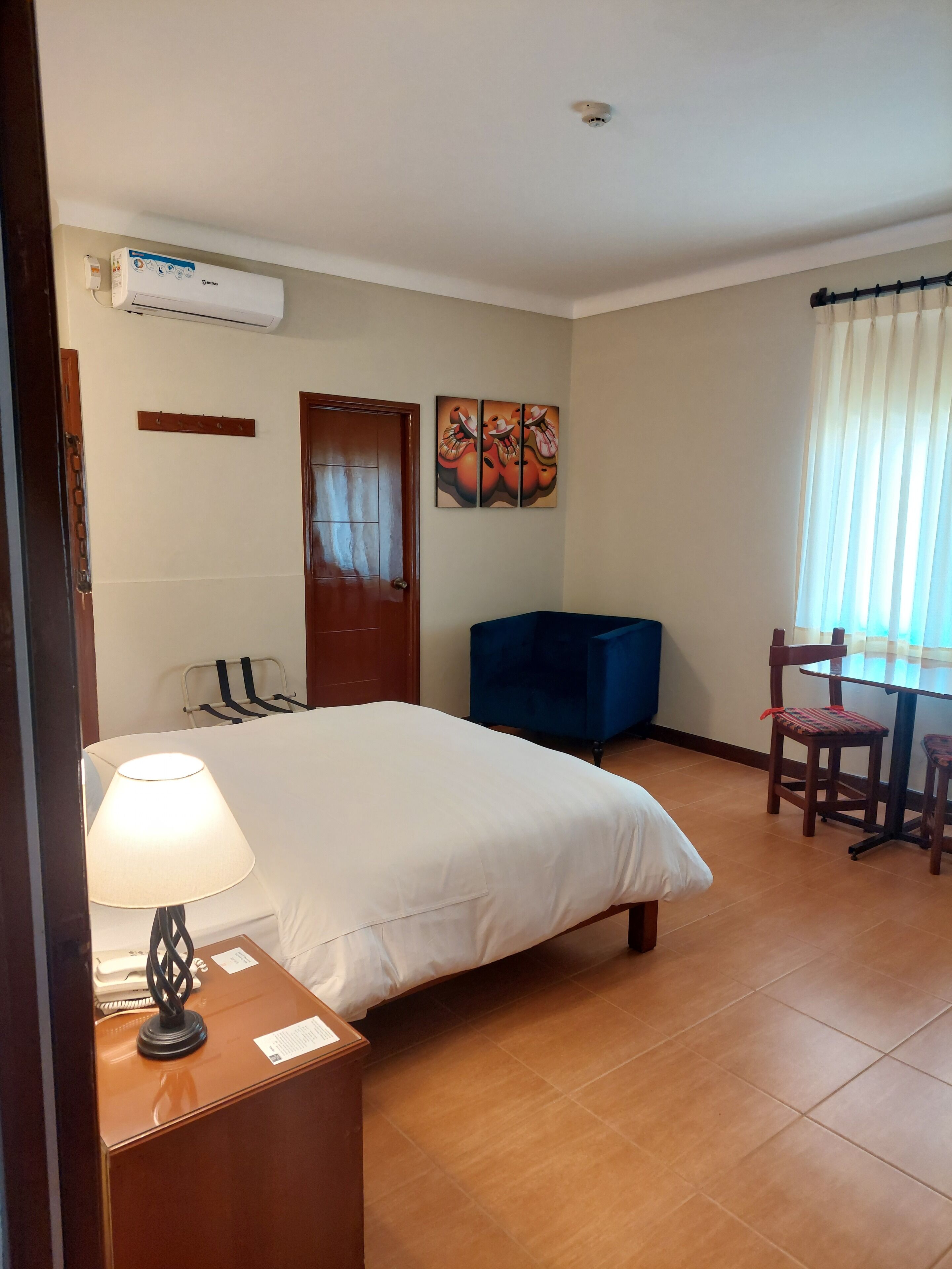 Ein Hotelzimmer mit einem Bett, einem Schreibtisch mit Lampe, einem Sessel, einem blauen Sofa, einer Tür und einer Wand-Klimaanlage.