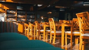 Un interior de restaurante con mesas y sillas de madera, una zona de bar y un área de estar con un sofá color turquesa.