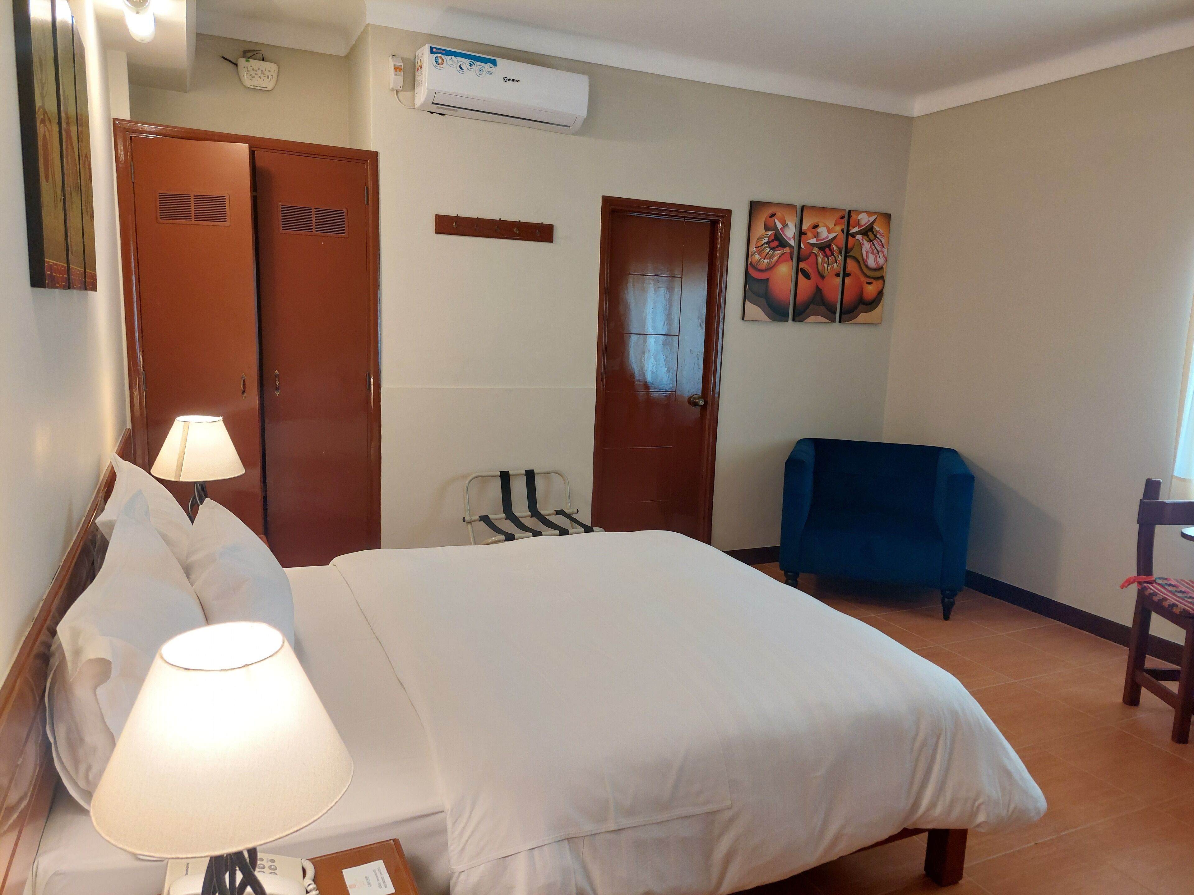 Ein Hotelzimmer mit einem Bett, einem Sessel, einem Schreibtisch mit Lampe, einem Kleiderschrank und einer Klimaanlage.