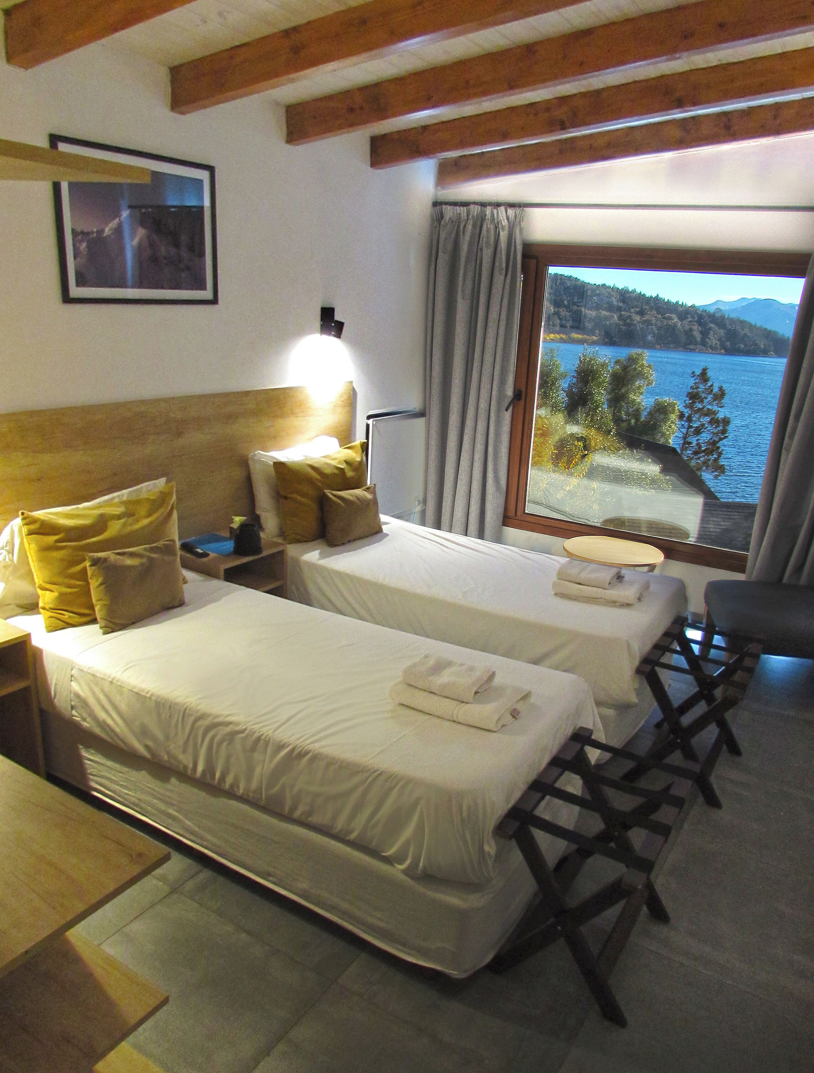 Une chambre d’hôtel avec deux lits, une tête de lit en bois, une table de chevet, un bureau et une vue sur un lac.