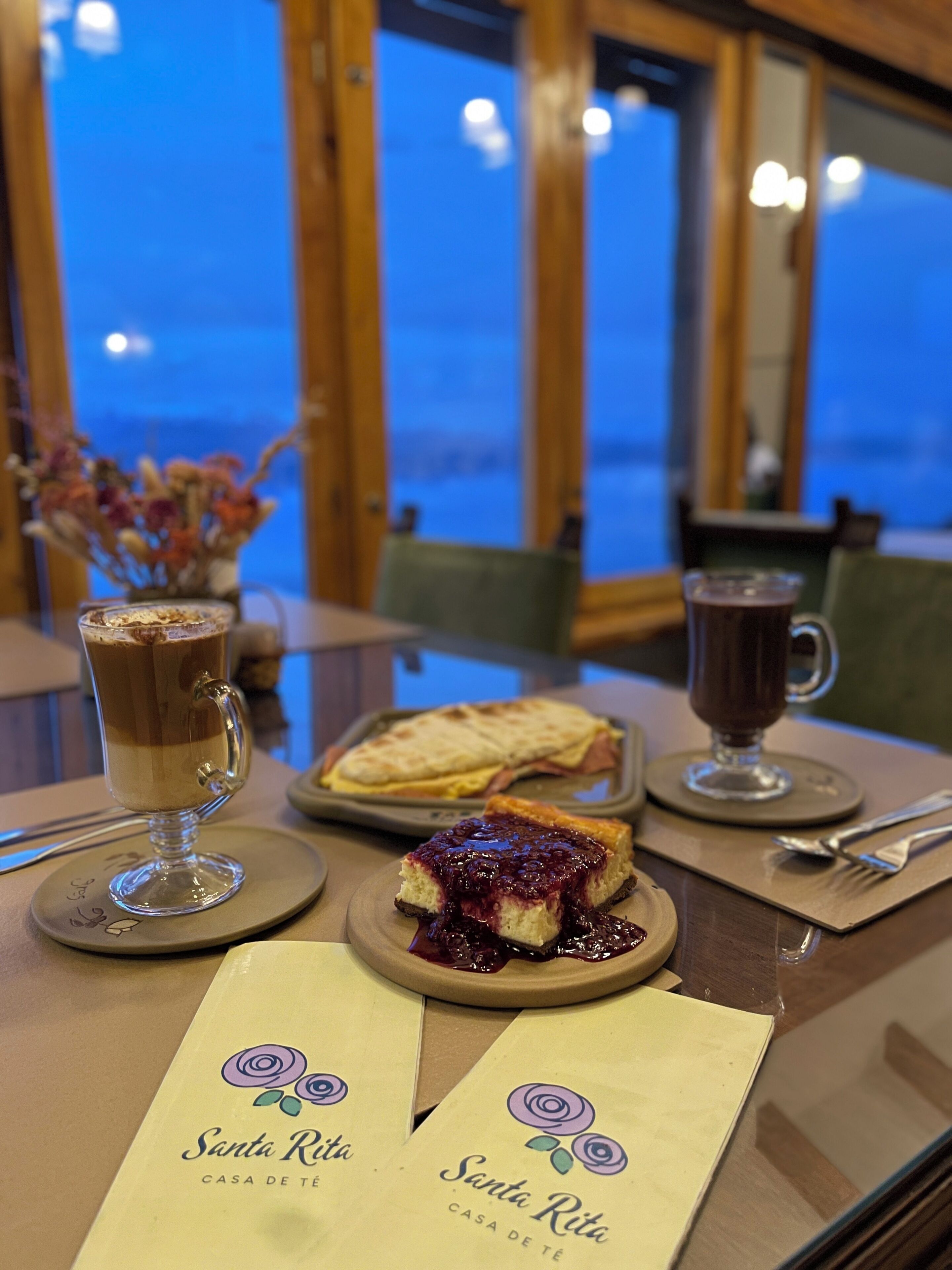 A table with a dessert, a coffee cup, and a plate of food, with a view of the sea in the background.