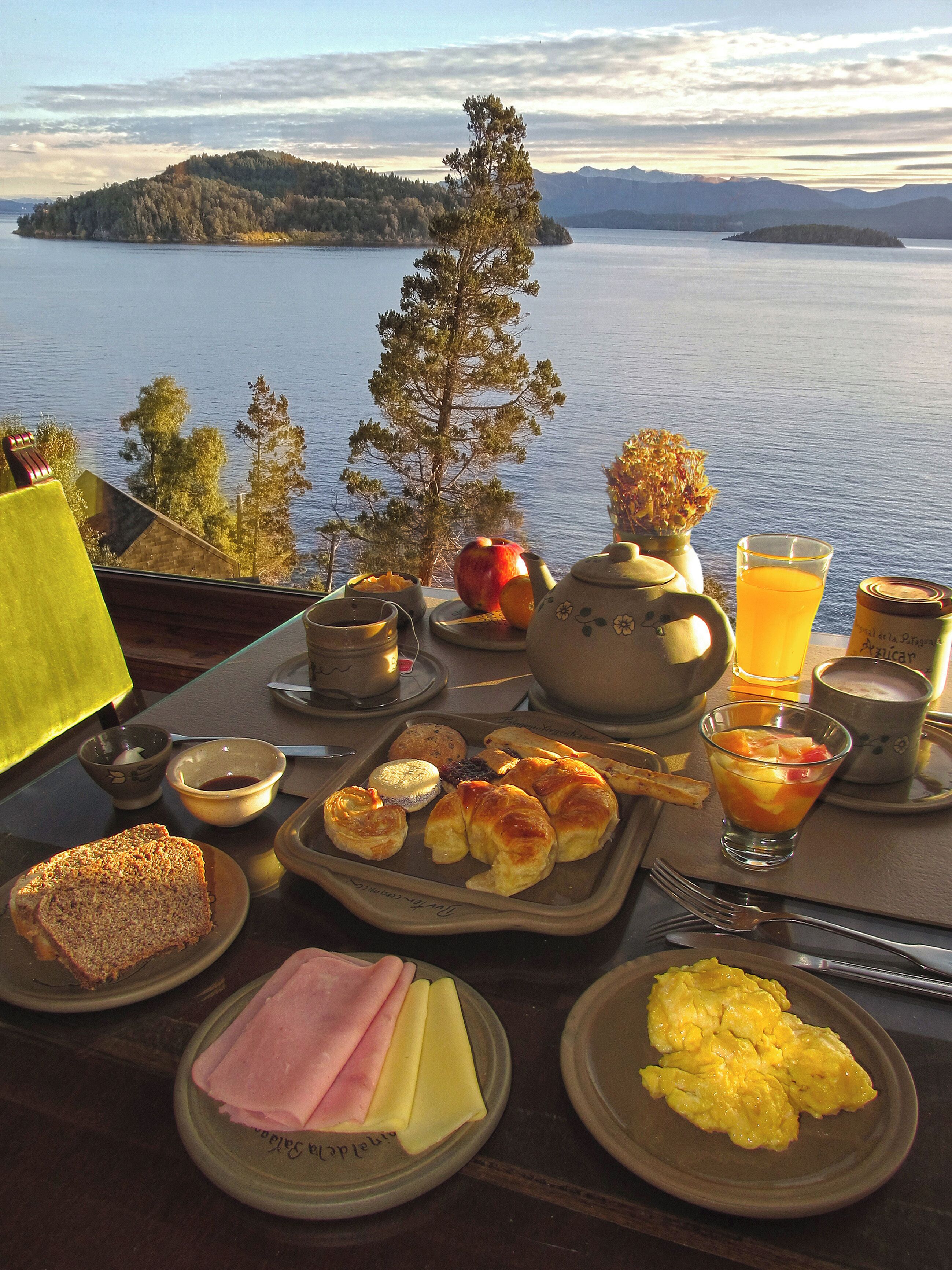 Una mesa de desayuno con diferentes alimentos y vistas a un lago y montañas.