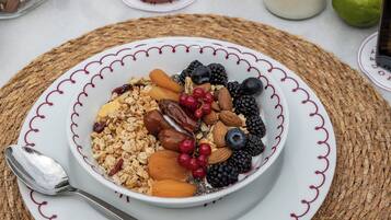 A breakfast setting with a bowl of granola, berries, and nuts on a woven placemat.