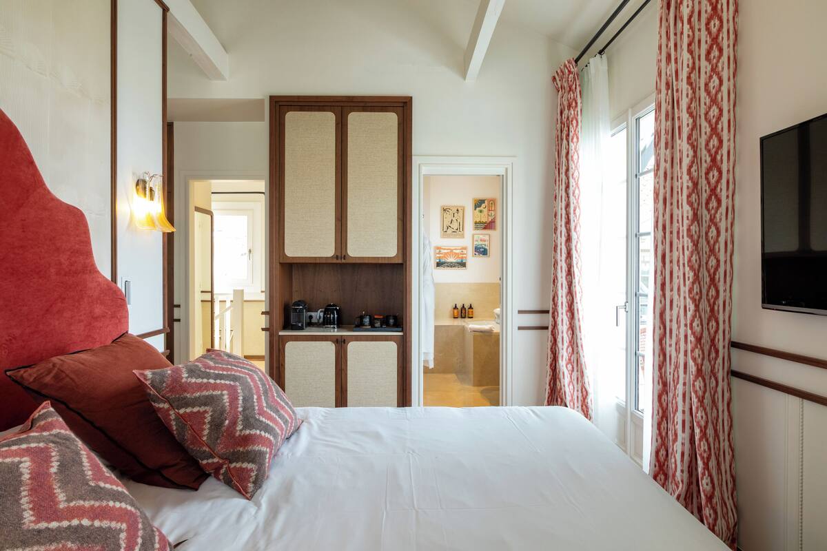 A bedroom with a bed, pillows, a wardrobe, a television, and a bathroom visible through an open door.