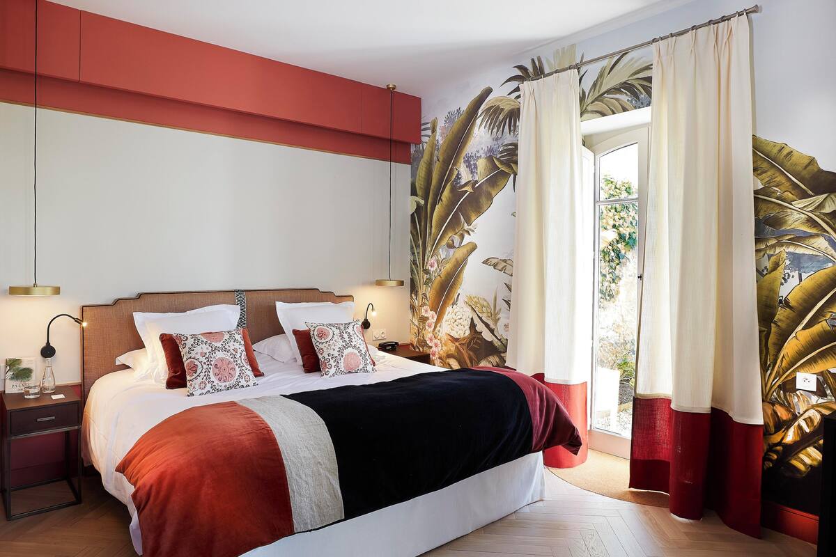 A bedroom with a large bed, a nightstand with a lamp, and a window with curtains.