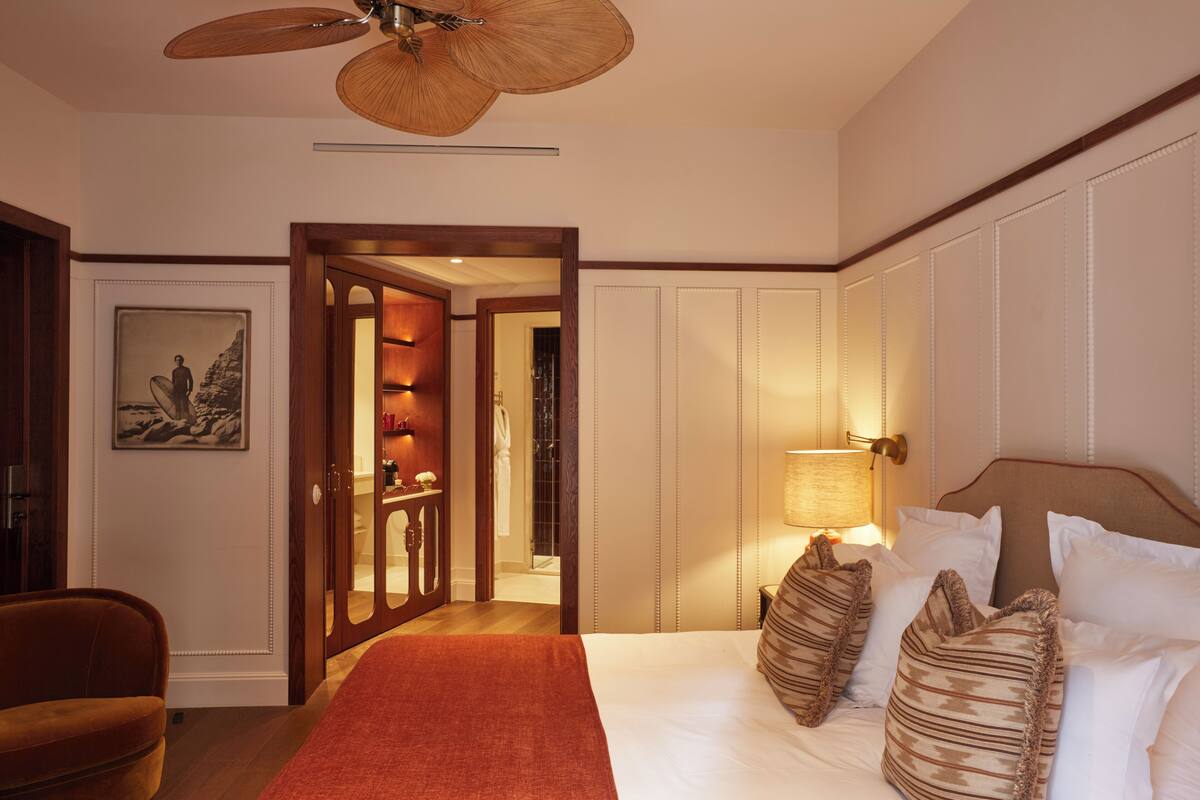 A hotel room with a bed, a wooden door, a ceiling fan, and a framed picture on the wall.