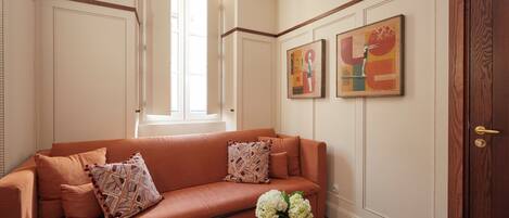 Una sala de estar con un sofá, almohadones decorativos, un jarrón con flores y dos cuadros en la pared.