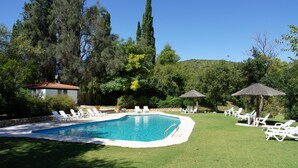 A swimming pool with lounge chairs and umbrellas, surrounded by trees and a hill in the background.