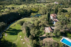 Vista aérea de um campo de golfe com uma casa grande e uma piscina.