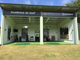 Academia de golf al aire libre con zona de estar techada, varios palos de golf y césped verde.