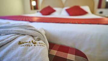 A hotel room with a bed featuring a red and white checkered bedspread, a white headboard, and red pillows. A white bathrobe with embroidered text is draped over the bed.