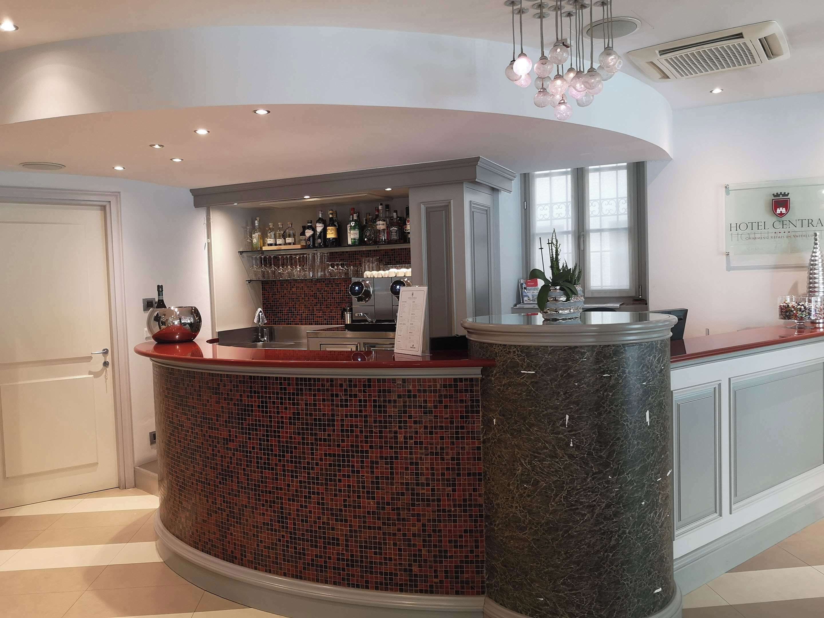 Zona de bar de un hotel con una barra curva de mármol, un salpicadero de azulejos y una variedad de botellas y vasos en estantes.