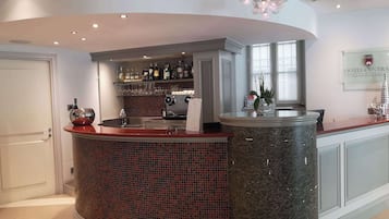 Zona de bar de un hotel con una barra curva de mármol, un salpicadero de azulejos y una variedad de botellas y vasos en estantes.