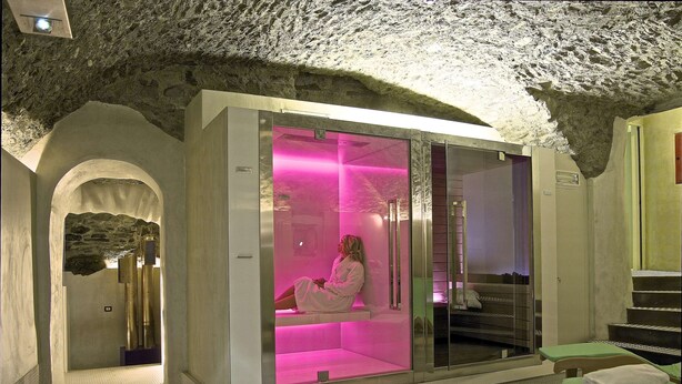 Un cuarto de spa con techo de piedra, una silla de masaje iluminada en tonos rosados y una zona de recepción con una escalera.